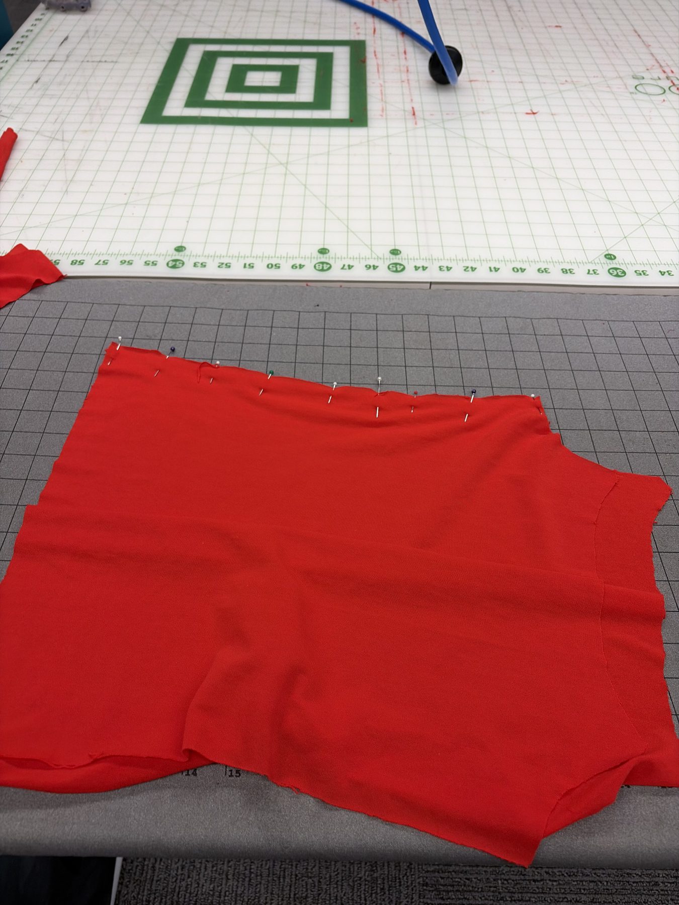 Red knit fabric pieces pinned together on a cutting mat